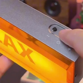 A gray box with a button and volume buttons. It glows orange and says "RELAX". Someone's finger is pressing the button.