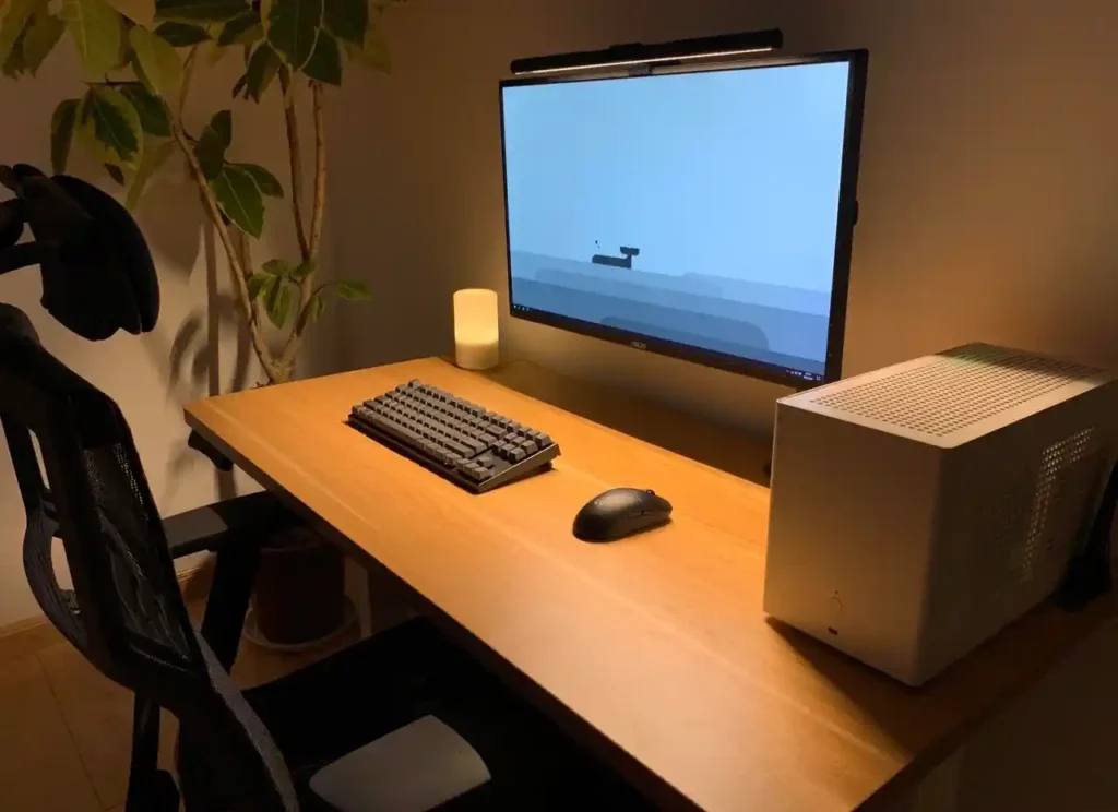 A cozy home office setup featuring a wooden desk, mechanical keyboard, large monitor, and a white computer tower, complemented by an indoor plant and a warm ambient light.