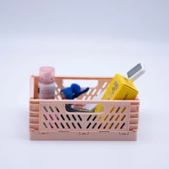 A pink plastic foldable organization basket filled with some small items