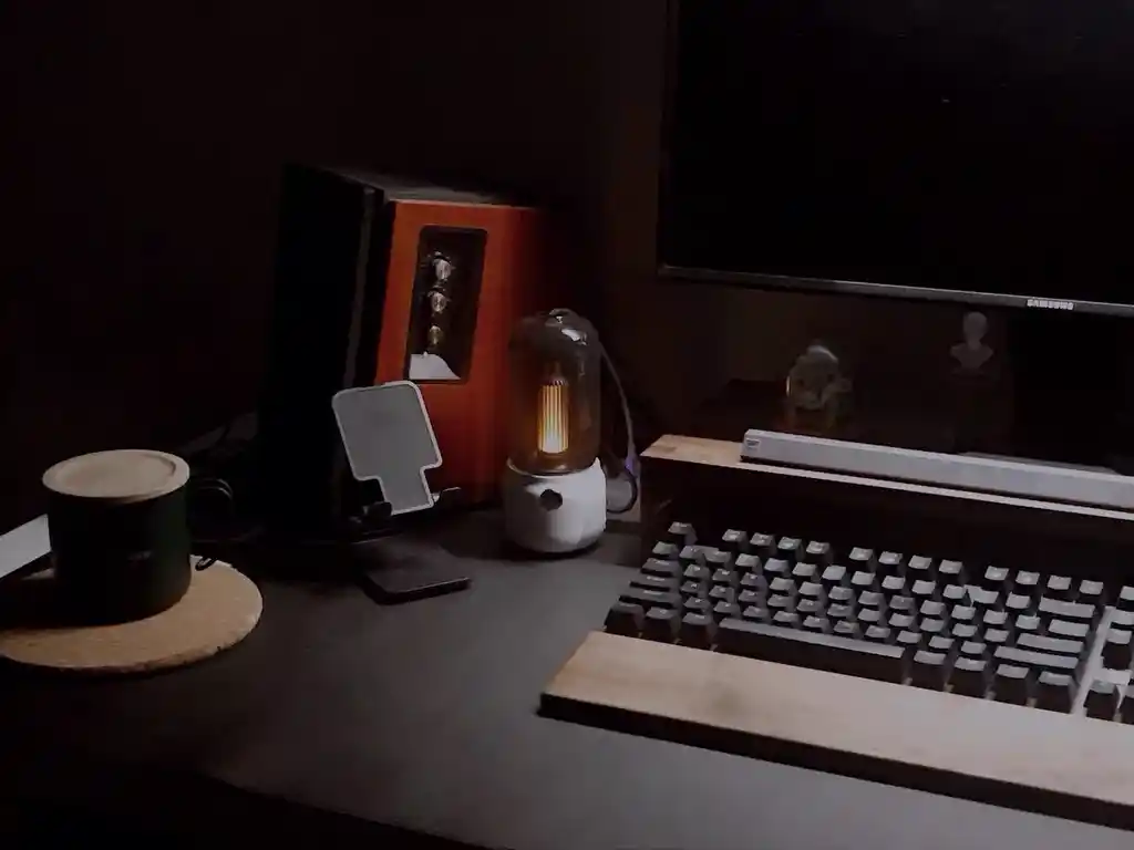 A dark room with a computer, keyboard, old lamp, and picture frame.