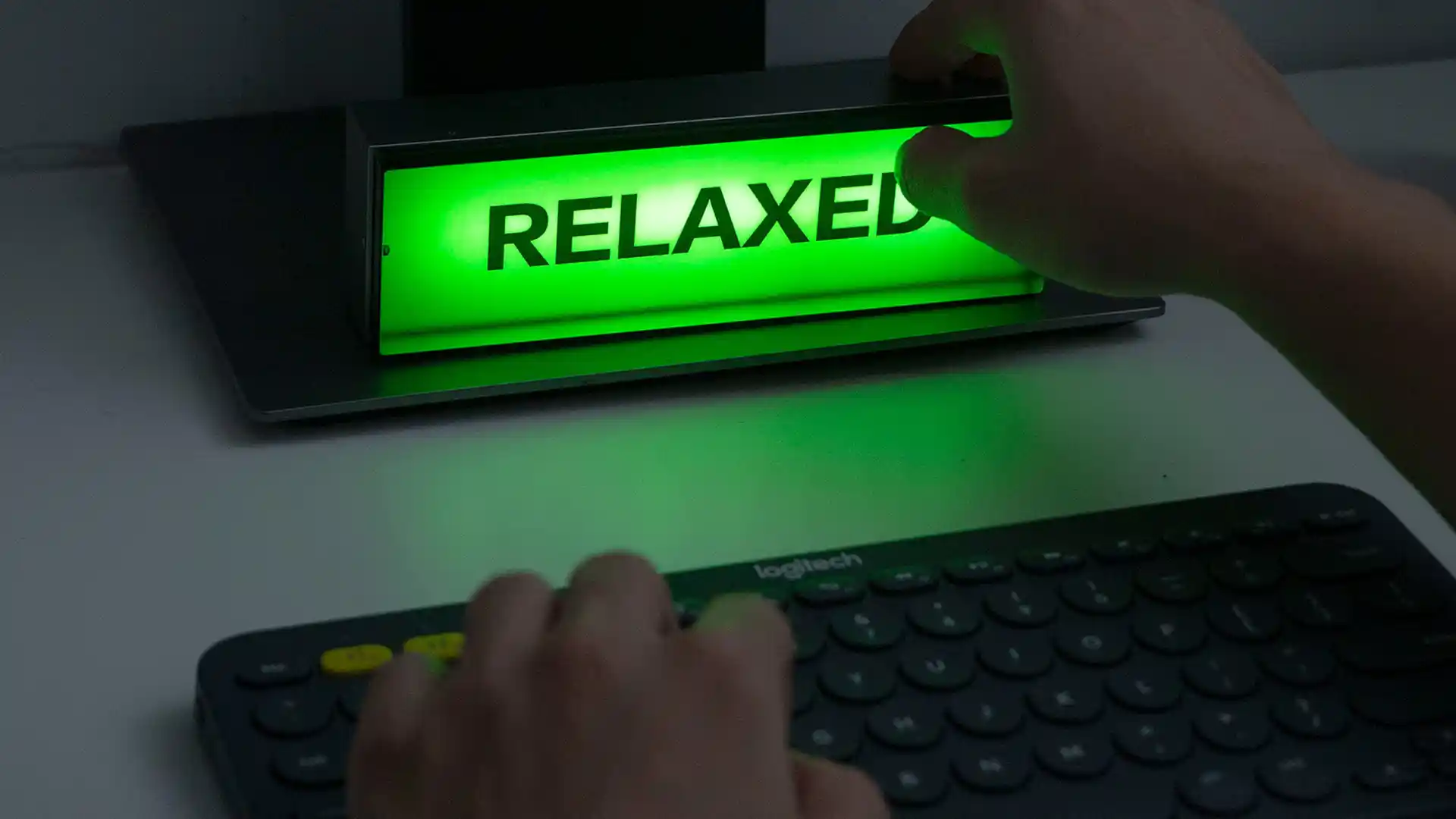 A close-up view of a keyboard and a lit-up green sign reading "RELAXED" with a hand reaching out.