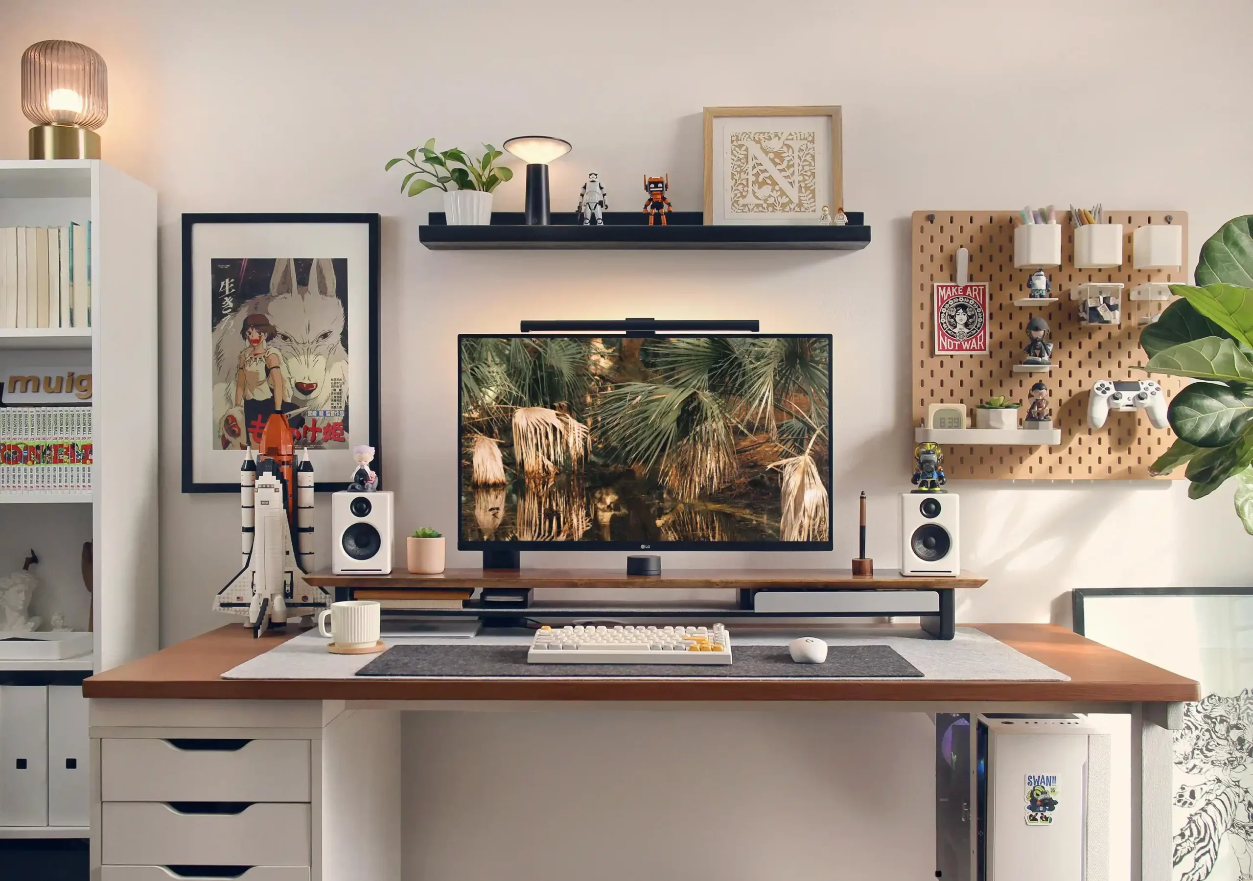 Stylish workspace setup with a desk featuring a computer monitor, various decorations, and a framed poster from the movie 'Princess Mononoke' on the wall.