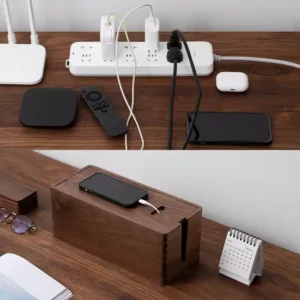 A wooden desk with various electronic devices including a power strip, phone chargers, a remote, and a wooden phone docking station.